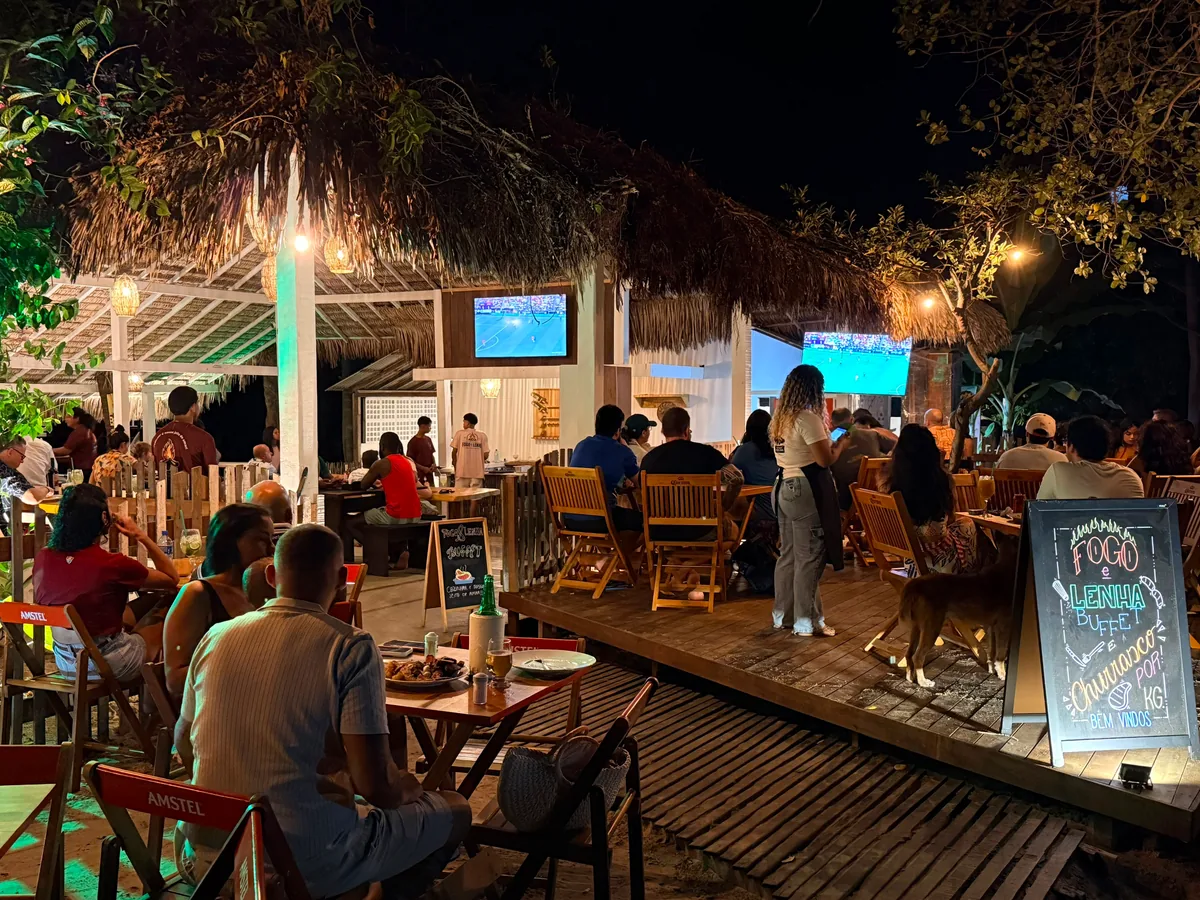 O salão do Fogo e Lenha à noite, cheio de gente, com o quadro do buffet e do churrasco